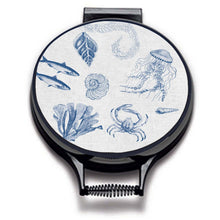 Load image into Gallery viewer, blue illustrations of sealife including fish, seaweed, shells, crabs, jelly fish, and fossilson a beige linen circular aga cover with black hemming. Pictured on metal aga lid on an isolated background. Mustard and Gray
