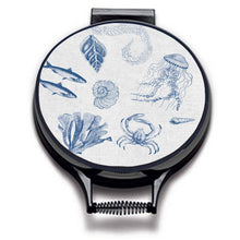 Load image into Gallery viewer, blue illustrations of sealife including fish, seaweed, shells, crabs, jelly fish, and fossilson a beige linen circular aga cover with black hemming. Pictured on metal aga lid on an isolated background. Mustard and Gray
