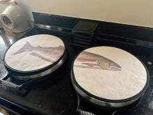 Load image into Gallery viewer, Set of two. painted illustration of a salmon fish with green and pink colouring print on a beige linen circular aga cover with black hemming. Fish head on one aga chef's pad and fish tail of the other aga chef's pad. Pictured on an AGA range cooker. Mustard and Gray Severn Salmon Circular Hob Cover