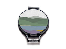 Load image into Gallery viewer, Simple landscape illustration of hills, lake and foreground of purple heather and yellow gorse printed onto neutral linen circular hob covers and hemmed in black. Pictured as aga chef's pads on aga lids with an isolated background. Aga pads from Mustard and Gray