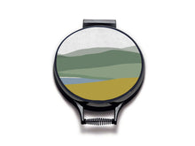 Load image into Gallery viewer, Simple landscape illustration of hills, lake and foreground of purple heather and yellow gorse printed onto neutral linen circular hob covers and hemmed in black. Pictured as aga chef's pads on aga lids with an isolated background. Aga pads from Mustard and Gray