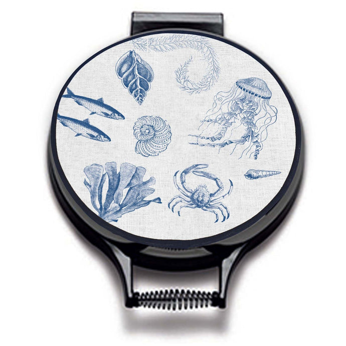 blue illustrations of sealife including fish, seaweed, shells, crabs, jelly fish, and fossilson a beige linen circular aga cover with black hemming. Pictured on metal aga lid on an isolated background. Mustard and Gray